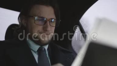 英俊的男子，棕色头发，穿着开心果衬衫，灰色外套，坐在车里，戴着眼镜看文件